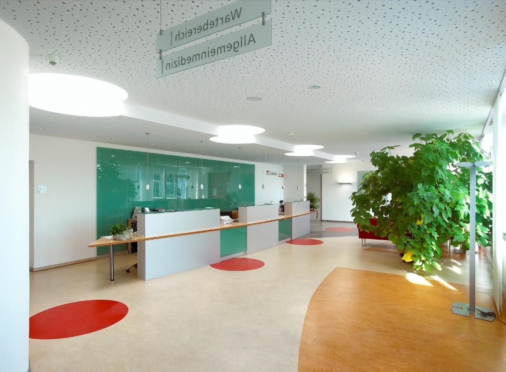 Moderner Empfangsbereich mit farbigen Naturböden und großer Glasfront Heller Empfangsbereich mit Linoleum-Naturboden in verschiedenen Farbzonen, Pflanzen und moderner Einrichtung